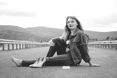 Portrait of young woman sitting on railing against sky