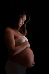 Side view of pregnant woman standing against black background