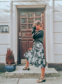 Woman standing close to a brown bbeautiful door, putting her hand in the head