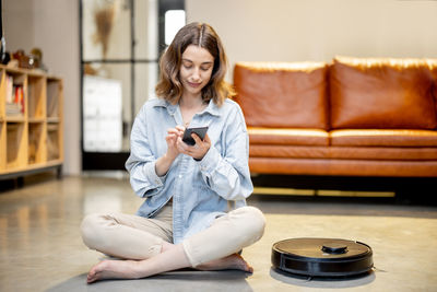 Young woman using phone while sitting on sofa at home