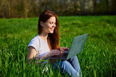 Young woman using laptop while sitting on field