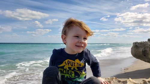 Smiling boy sitting at beach against sky