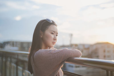 Side view of young woman looking away against sky