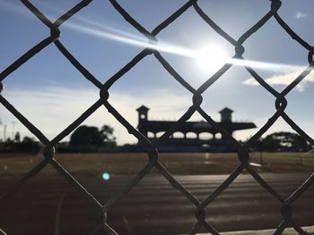 Close-up of chainlink fence against sky during sunny day