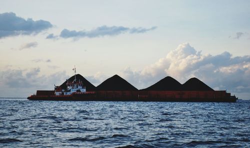 Stilt house by sea against sky during sunset