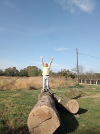 Portrait of man standing log with arms raised against sky