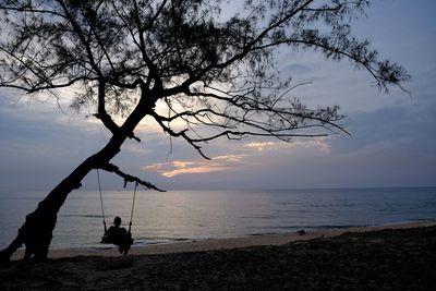 Silhouette people relaxing on beach against sky during sunset