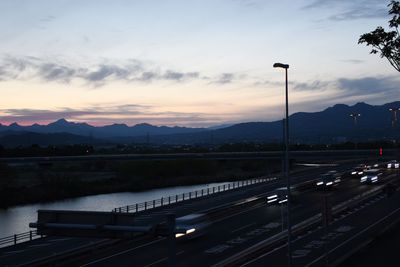 Vehicles on road against sky during sunset