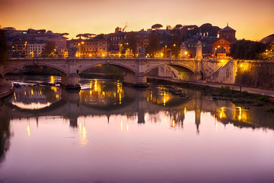 Old arch bridge over tiber river in illuminated town against sky during sunset