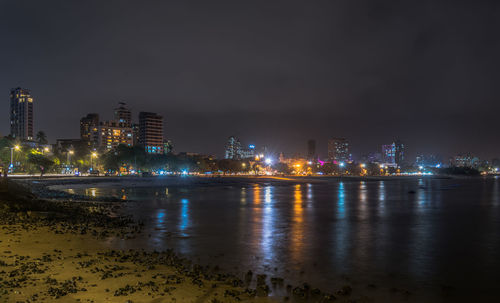Illuminated buildings by river against sky at night