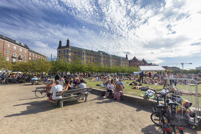 People at park by buildings against sky in city