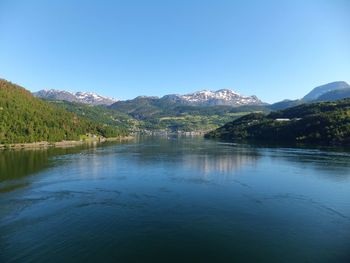 Scenic view of lake and mountains against clear blue sky