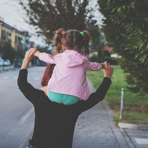 Rear view of grandmother carrying granddaughter on shoulder on street