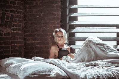 Young woman wearing bikini lying on bed against window at home