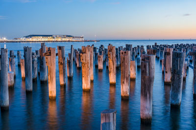 View of wooden posts in sea against clear sky during sunset