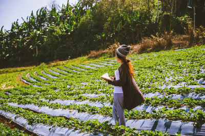 Woman wearing knit hat holding book while standing on field