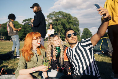 Young man taking selfie with friends on smart phone during music concert in summer
