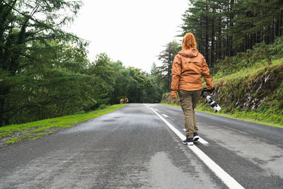 Unrecognizable caucasian female photographer walking along a road to take nature photos