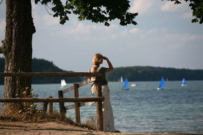 Rear view of woman standing by lake against sky