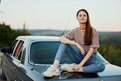 Portrait of young woman sitting on car