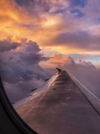 Cropped image of aircraft wing flying over clouds during sunset seen through airplane window