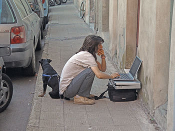 Side view of young woman by dog using laptop on footpath b