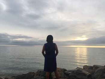 Rear view of man standing at sea shore against sky