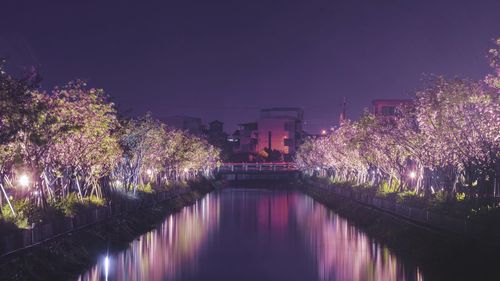 Illuminated bridge over river in city against sky at night