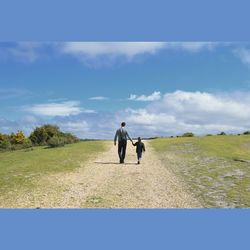 Full length of woman standing on grassy field against blue sky