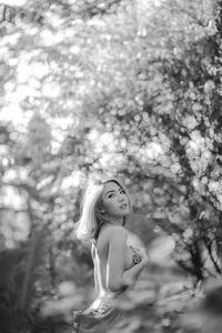 Side view of topless young woman looking away while standing against trees