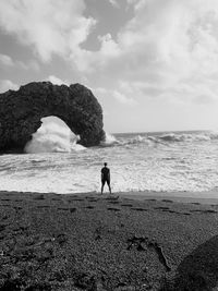 Man standing on a beach by sea against sky and massive rocks