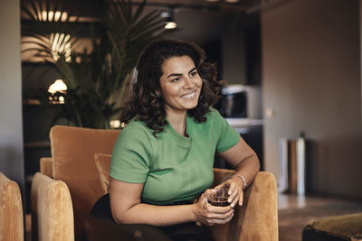 Smiling businesswoman with tea cup sitting on armchair in office