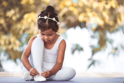 Full length of girl tying ballet shoelace against plants