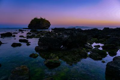 Rocks on sea shore against sky during sunset