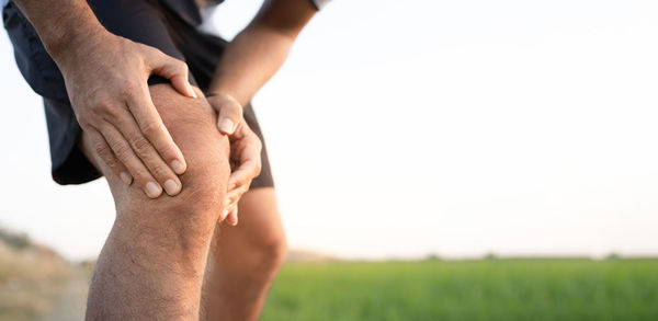 Midsection of man hand on field against sky