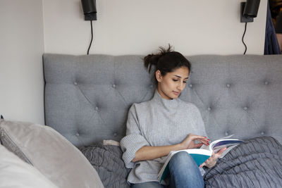 Young woman sitting on sofa and reading book