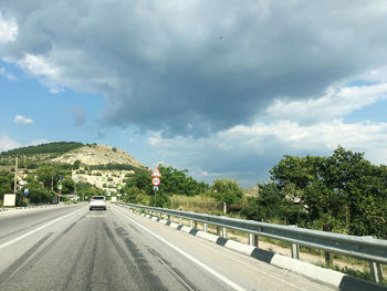 Road by trees against sky