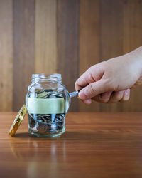 Cropped hand holding magnifying glass by jar with coins at table