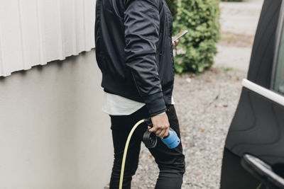 Midsection of man with electric car at charging station