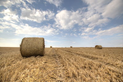 Hay bales on field against cloudy sky