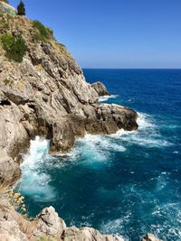 Rock formations in sea against clear blue sky