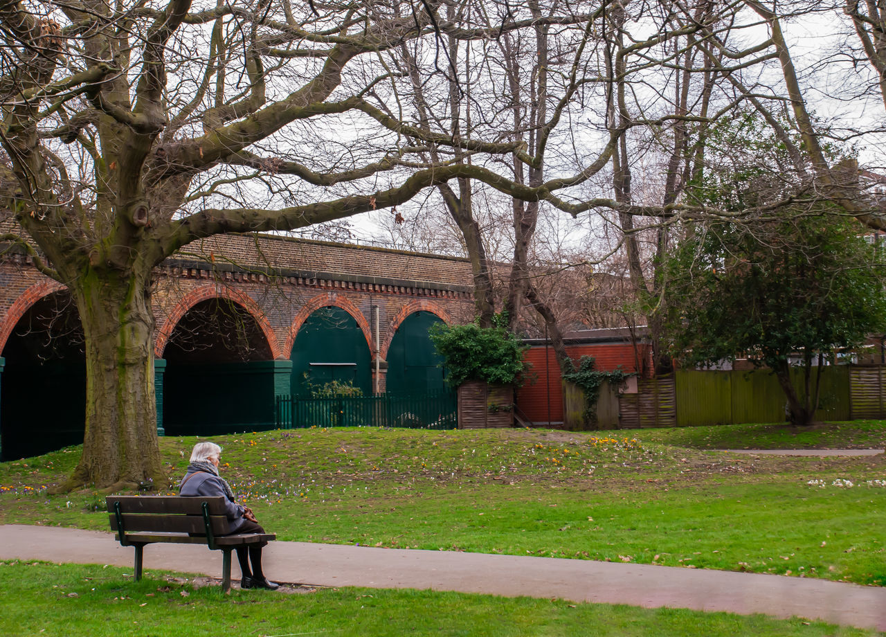 MAN SITTING ON BENCH IN PARK AGAINST BUILDINGS