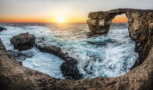 Scenic view of rock formation at sea shore against clear sky during sunset