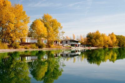 Scenic view of lake by trees and houses against sky