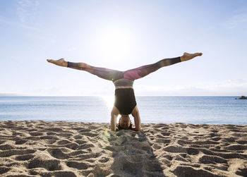 Young woman with legs apart performing headstand on beach