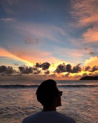 Rear view of silhouette woman standing at beach during sunset