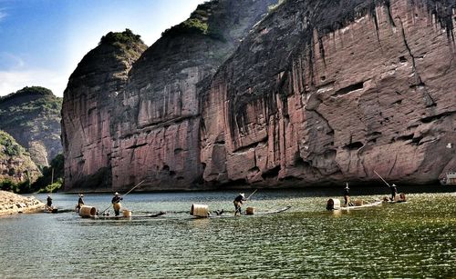 Fishermen with cormorant birds sailing boats in river against cliff