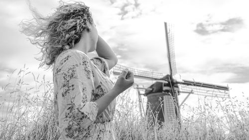 Low angel view of woman standing by windmill in farm