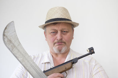 Close-up portrait of man with machete and gun against white background