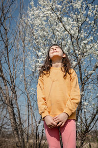 Low angle view of standing girl against sky and blooming trees
